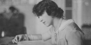 Maria Brydzińska w swoim mieszkaniu, siedząca przy stole z książką.