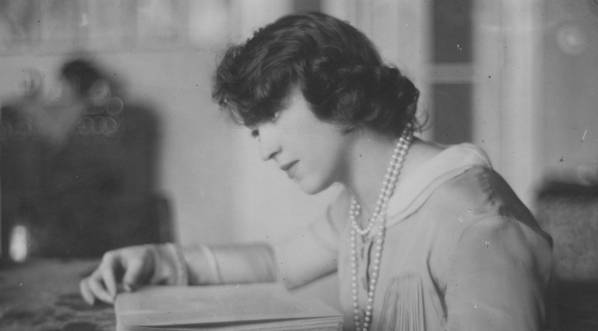  Maria Brydzińska w swoim mieszkaniu, siedząca przy stole z książką.  